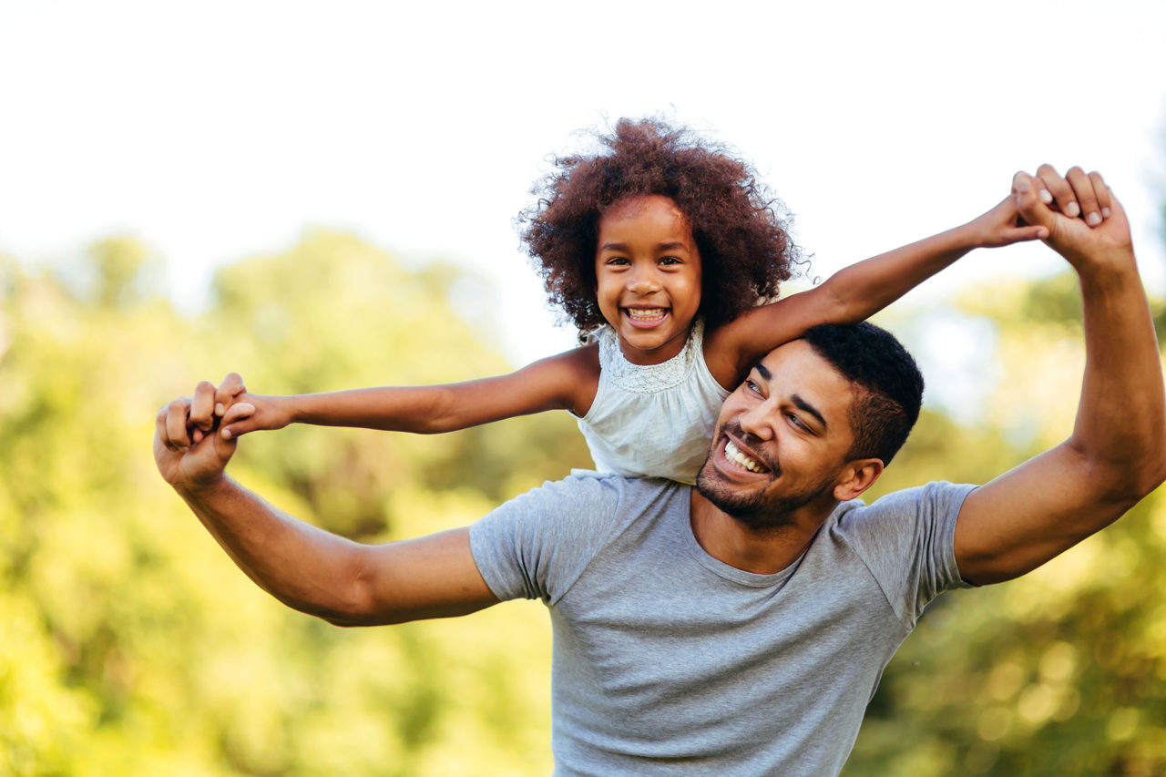 Portrait of young father carrying his daughter on his back in nature